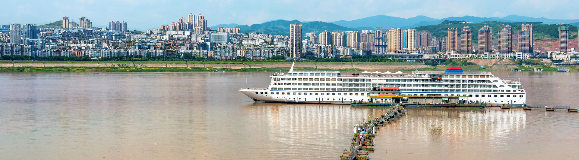 Yangtze cruise ship moored at a floating pier below a riverside city skyline
