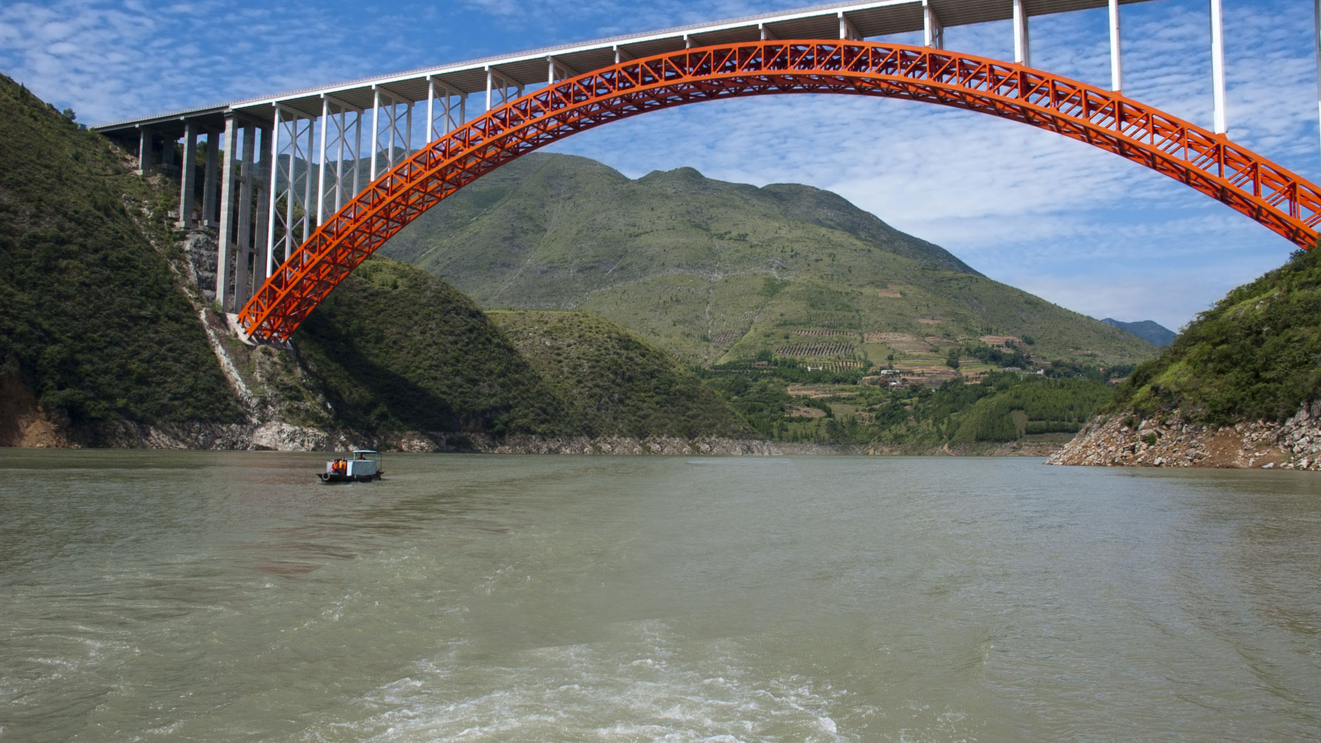 Red arch bridge spanning the river between steep green gorge walls