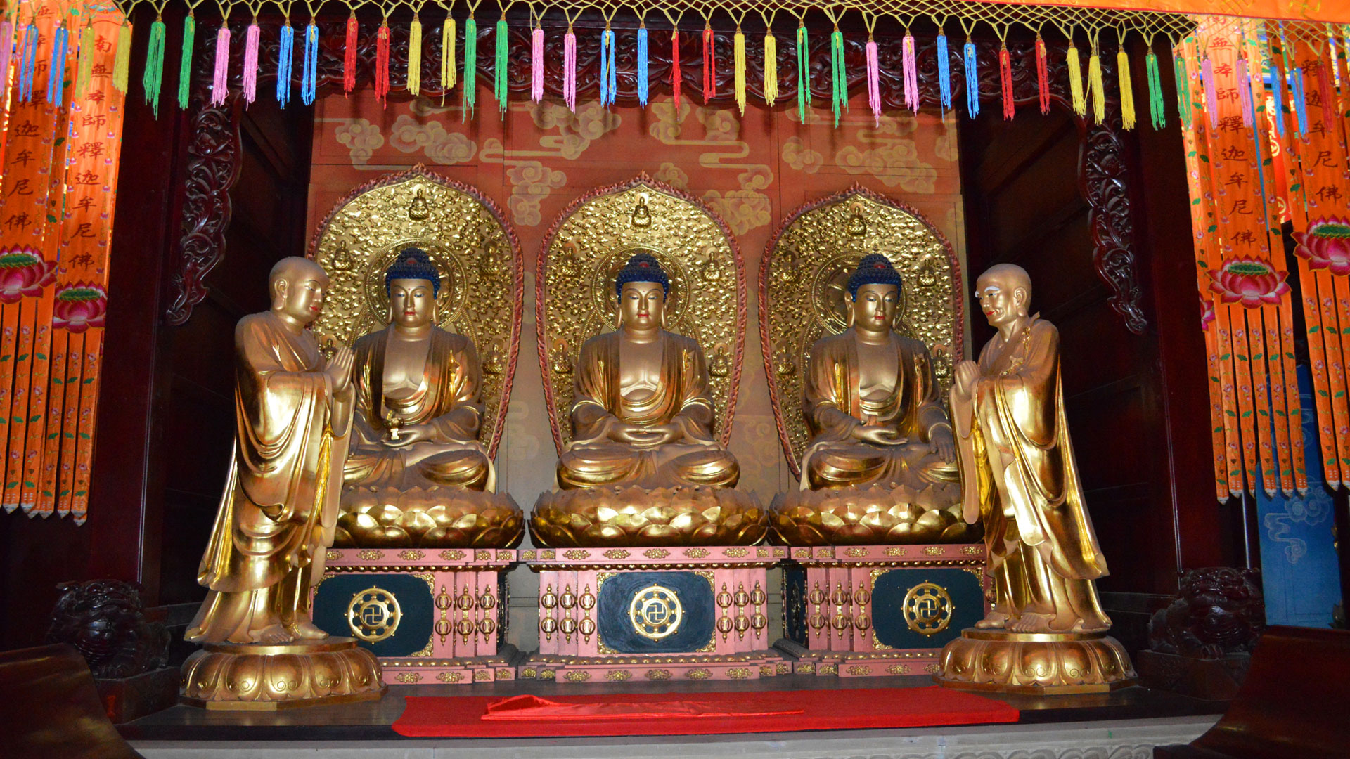 Row of gilded Buddha statues inside a colourful temple hall